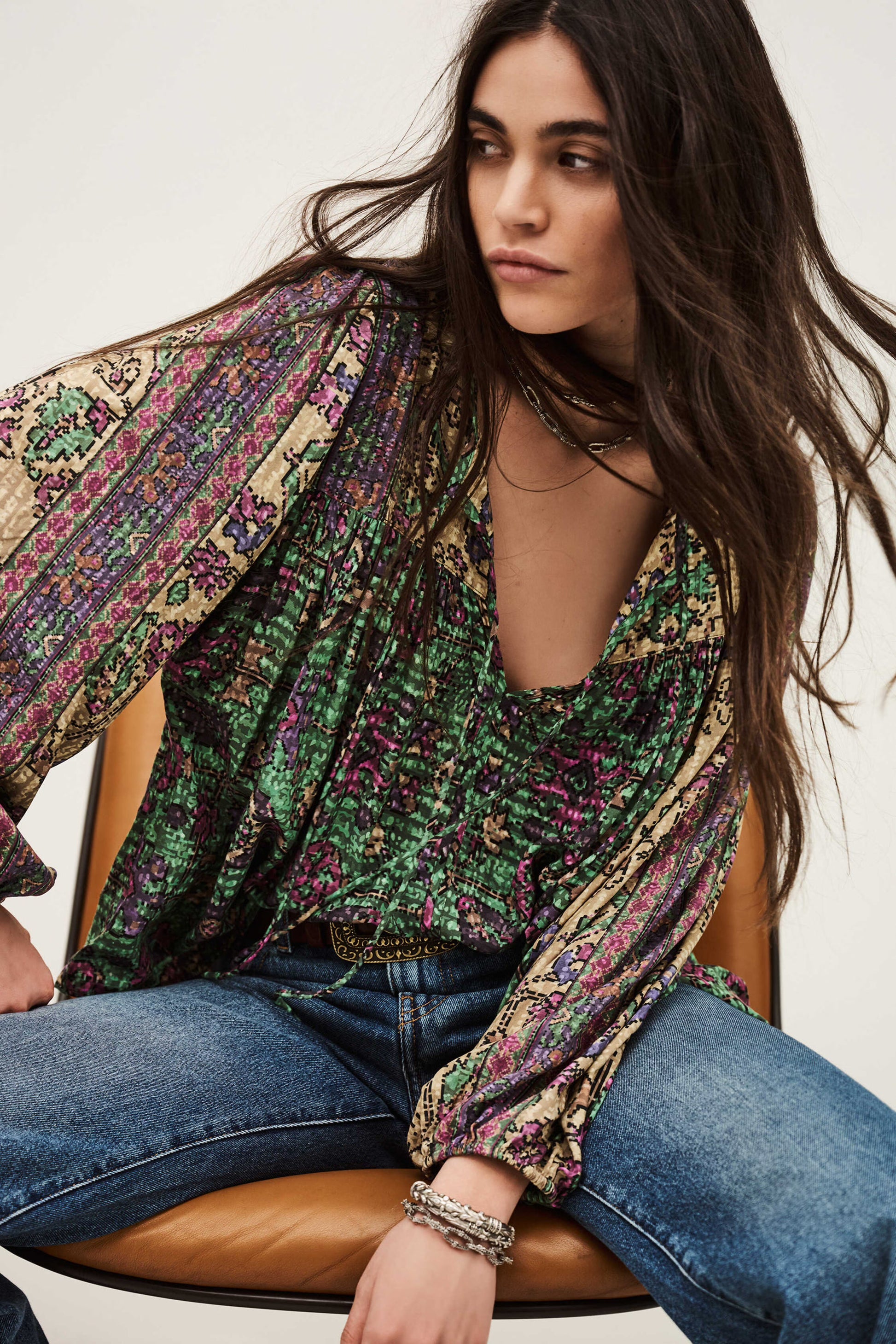 Woman wearing a patterned blouse and jeans sitting on a chair.