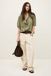 Woman wearing a green patterned blouse and beige pants, holding a brown bag on a white background from ba&sh