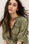 Woman wearing a green floral blouse with long hair against a neutral background from ba&sh