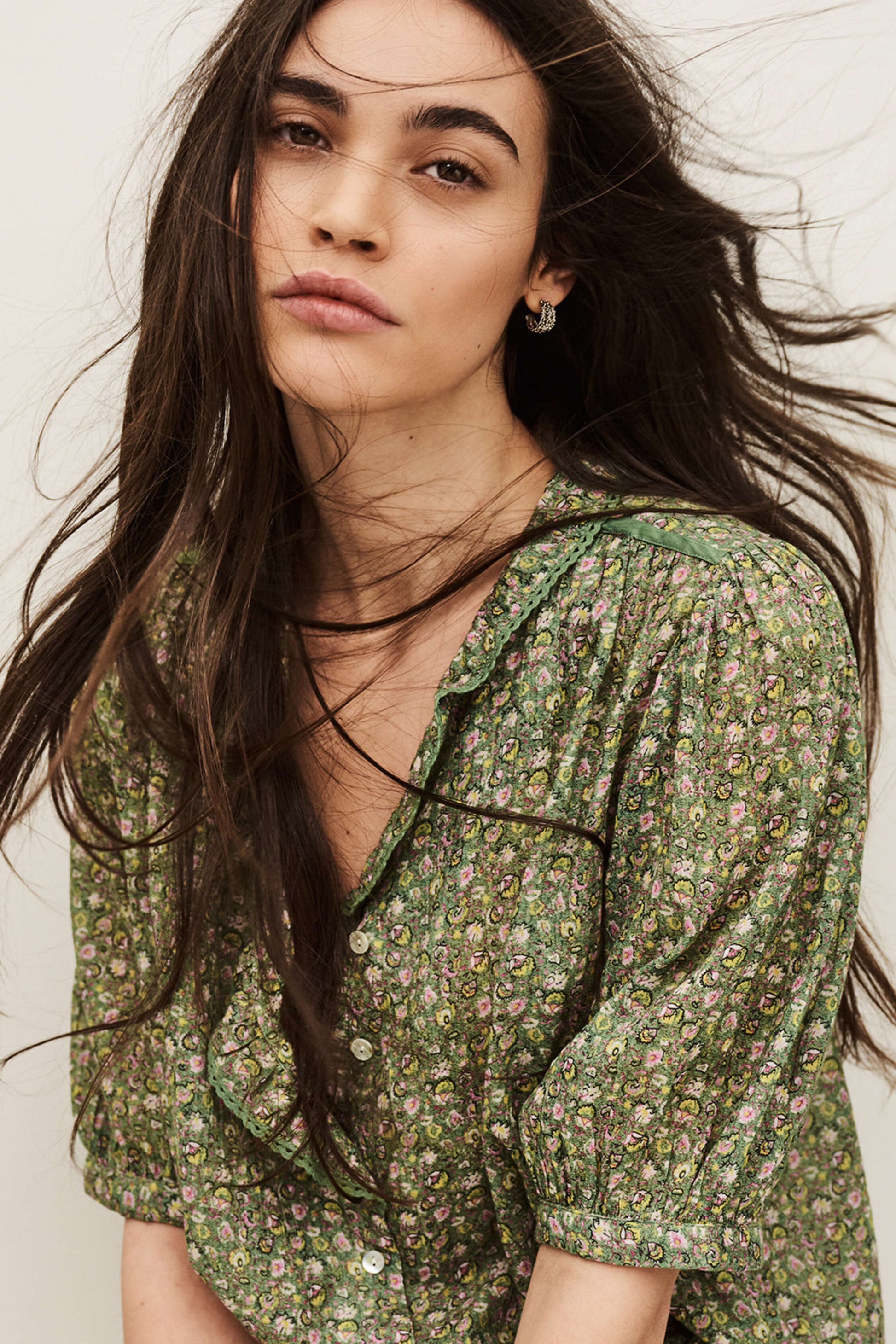 Woman wearing a green floral blouse with long hair against a neutral background from ba&sh