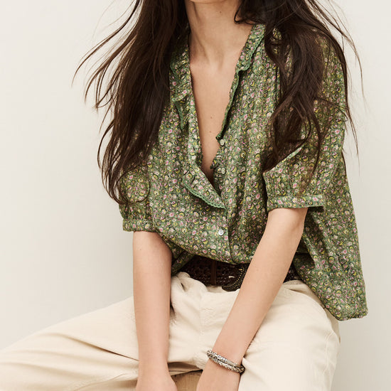 Woman wearing a green floral blouse and beige pants against a white background from ba&sh