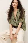 Woman wearing a green floral blouse and beige pants against a white background from ba&sh