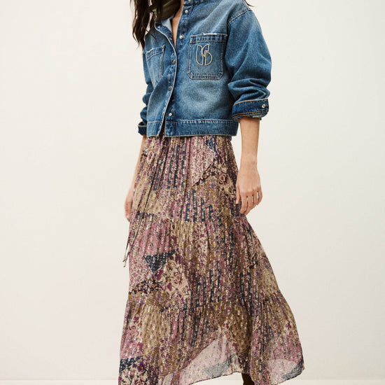 Woman wearing a denim jacket and patterned skirt on a white background
