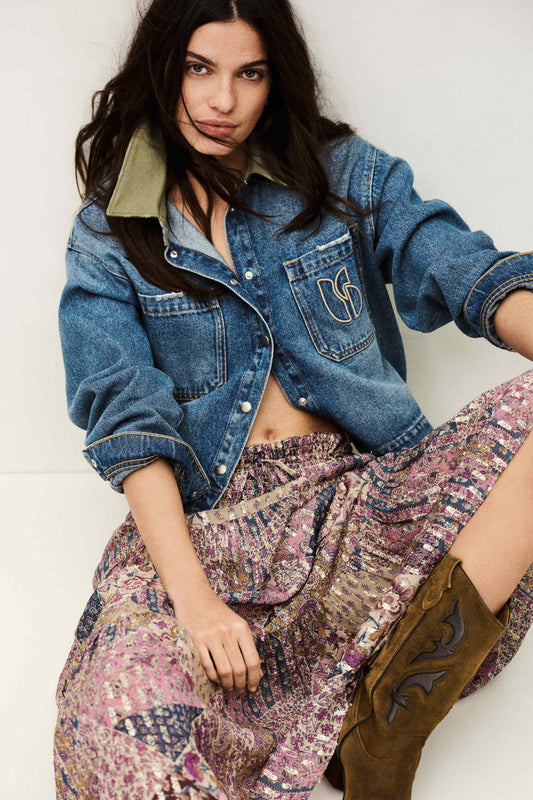 Woman wearing a denim jacket, patterned skirt, and brown boots against a white background