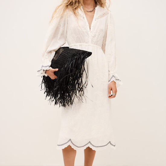 Woman in a white dress holding a black clutch against a white background from ba&sah