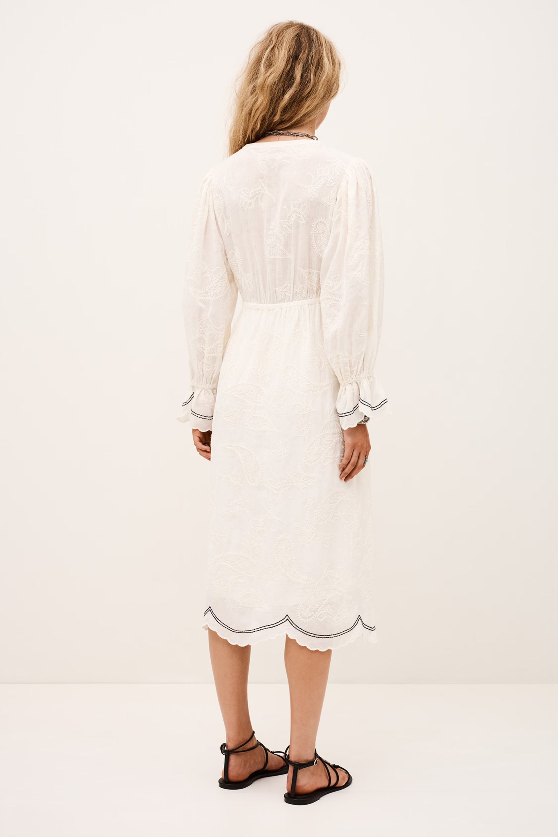 Woman wearing a white dress with long sleeves on a plain background rear view