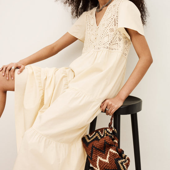Woman in a beige dress sitting on a black stool with a patterned bag.