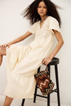 Woman in a beige dress sitting on a black stool with a patterned bag.