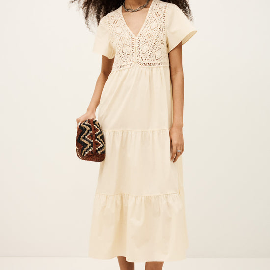 Woman wearing a beige dress holding a patterned clutch against a white background