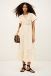 Woman wearing a beige dress holding a patterned clutch against a white background