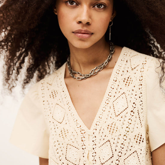 Woman wearing a beige lace top with a neutral background