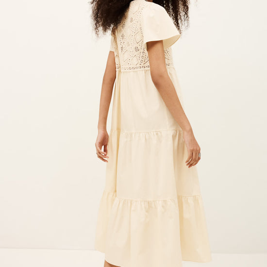 Woman wearing a cream-colored dress with lace details on a white background
