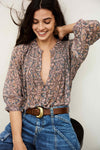 Woman wearing a patterned blouse and blue jeans with a white background from bash
