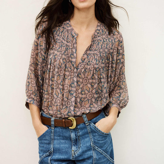 Woman wearing a patterned blouse and blue jeans against a plain background from bash