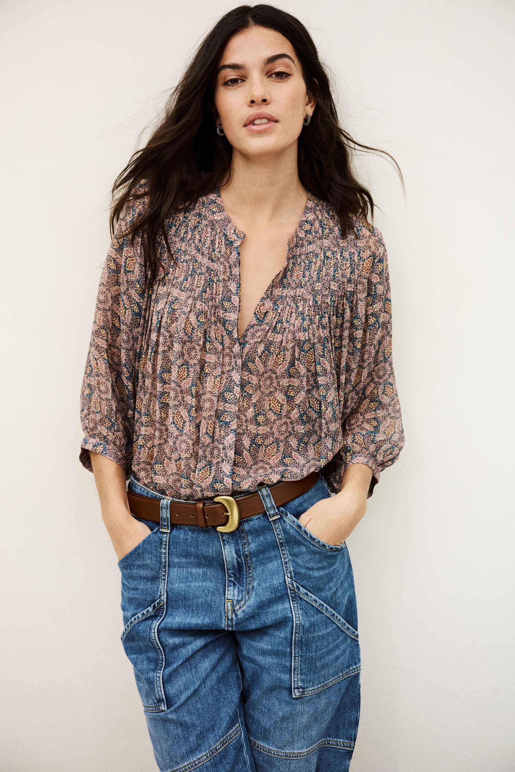 Woman wearing a patterned blouse and blue jeans against a plain background from bash