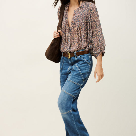 Woman wearing a patterned blouse, blue jeans, and brown shoes on a white background from bash