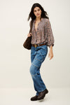 Woman wearing a patterned blouse, blue jeans, and brown shoes on a white background from bash