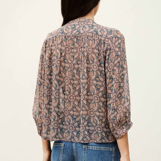 Person wearing a patterned blouse and jeans on a plain background from bash
