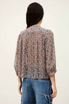 Person wearing a patterned blouse and jeans on a plain background from bash