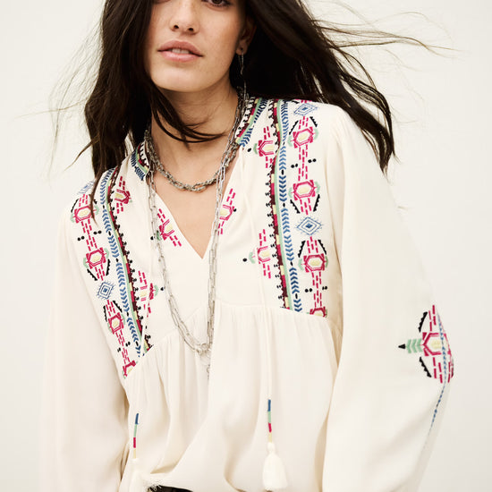 Woman wearing a white blouse with colorful patterns on a plain background