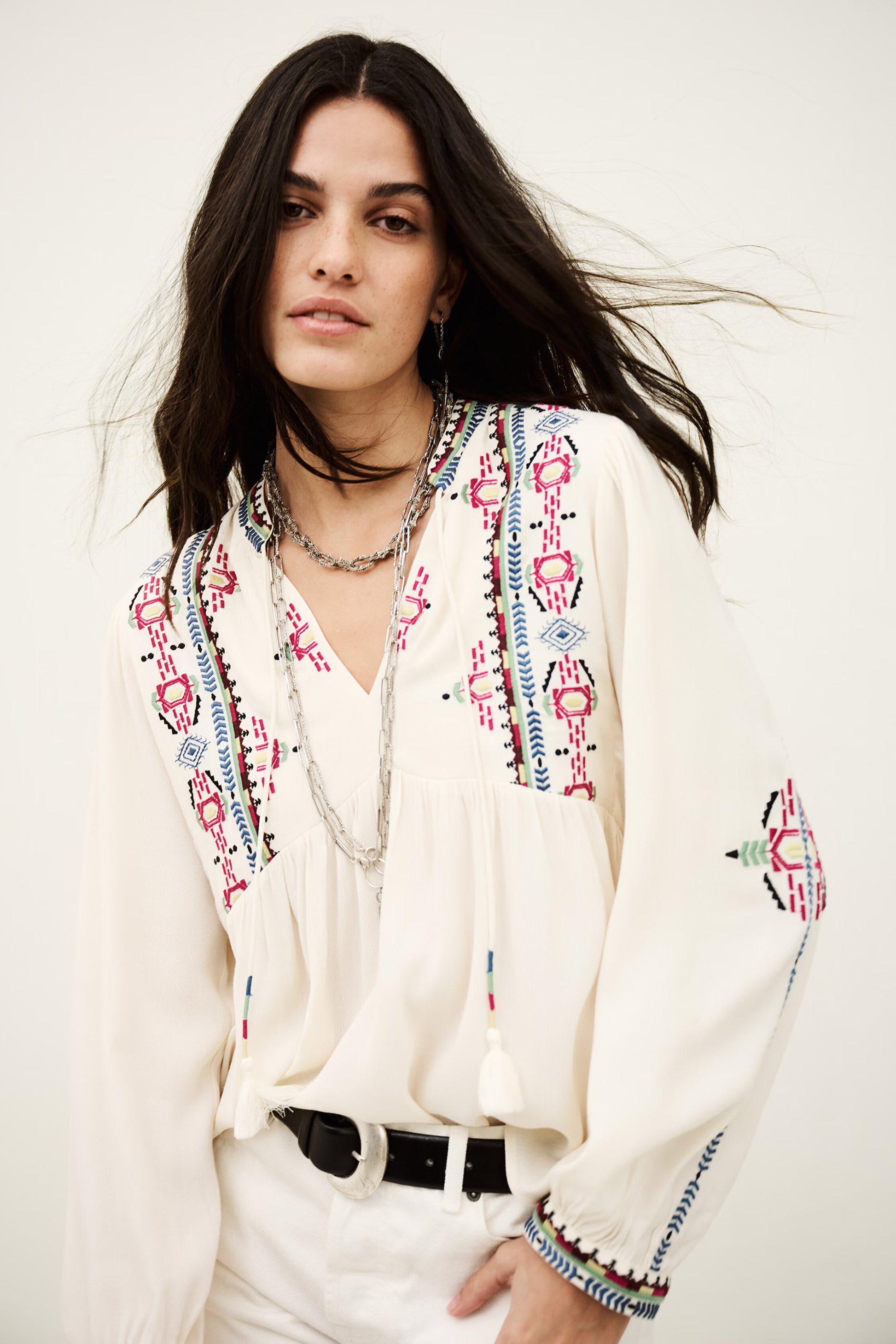 Woman wearing a white blouse with colorful patterns on a plain background