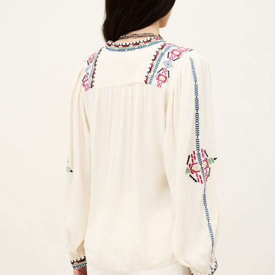 Woman wearing a white blouse with colorful embroidery on a white background