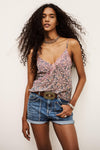 Woman wearing a patterned top and denim shorts against a plain background