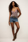 Woman wearing a floral top and denim shorts with a belt, standing against a plain background.