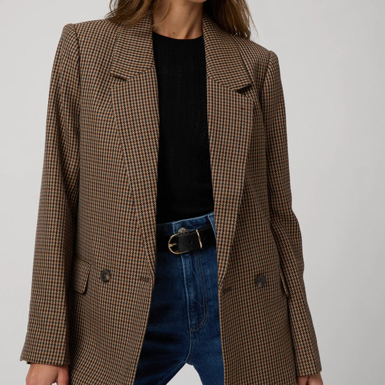 Person wearing a brown checkered blazer over a black top and blue jeans on a light gray background