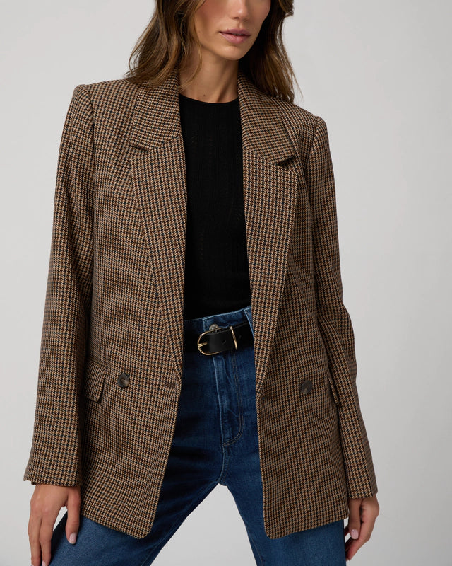 Person wearing a brown checkered blazer over a black top and blue jeans on a light gray background