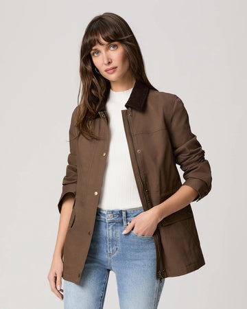 Woman wearing a brown jacket with a white shirt and blue jeans on a light gray background
