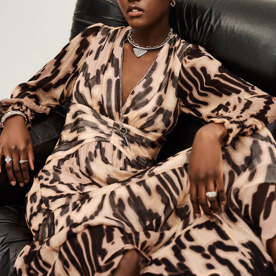 Woman wearing a leopard print dress sitting on a black leather chair.