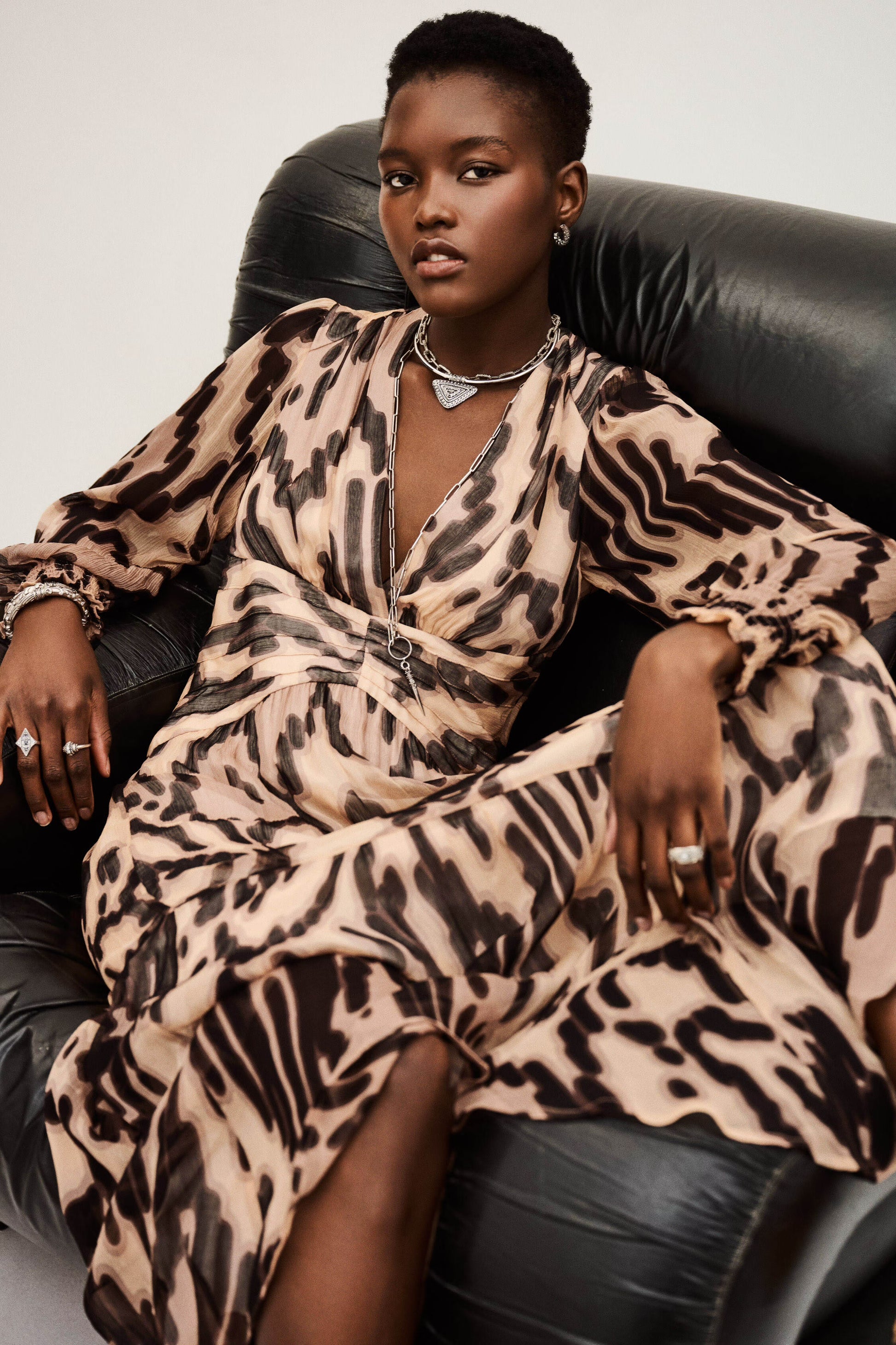 Woman wearing a leopard print dress sitting on a black leather chair.