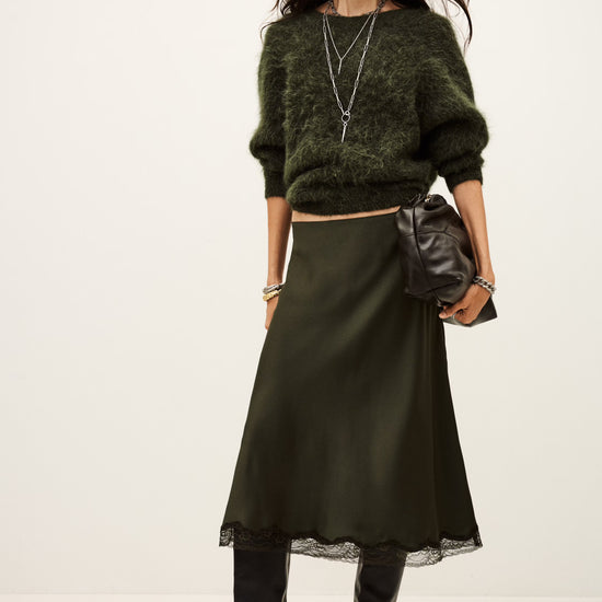 Woman wearing a green sweater, black skirt, and black boots on a white background from ba&sh