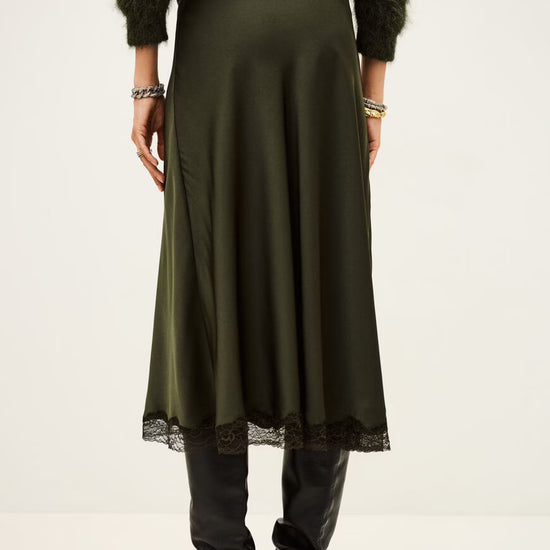 Person wearing a long green skirt with black shoes on a white from ba&shbackground