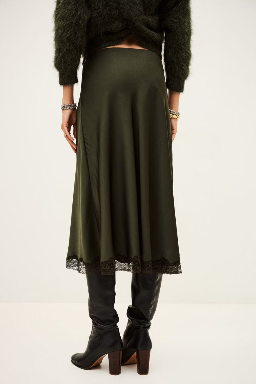 Person wearing a long green skirt with black shoes on a white from ba&shbackground