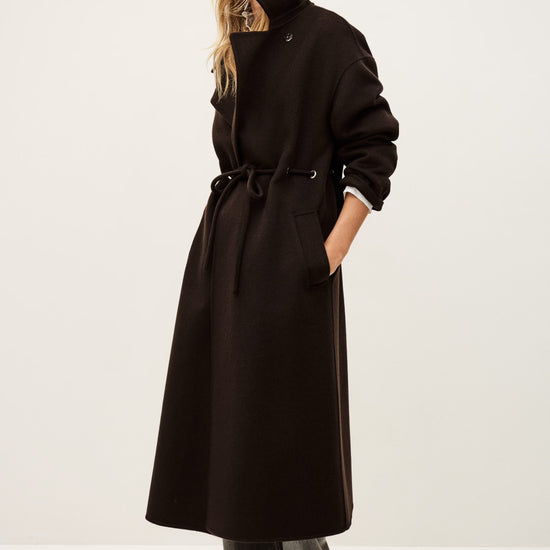 Person wearing a long brown coat and hat on a white background