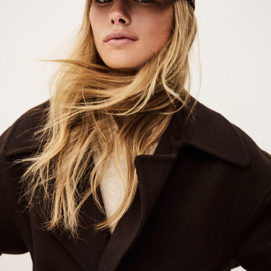 Woman wearing a brown coat and cap against a plain background