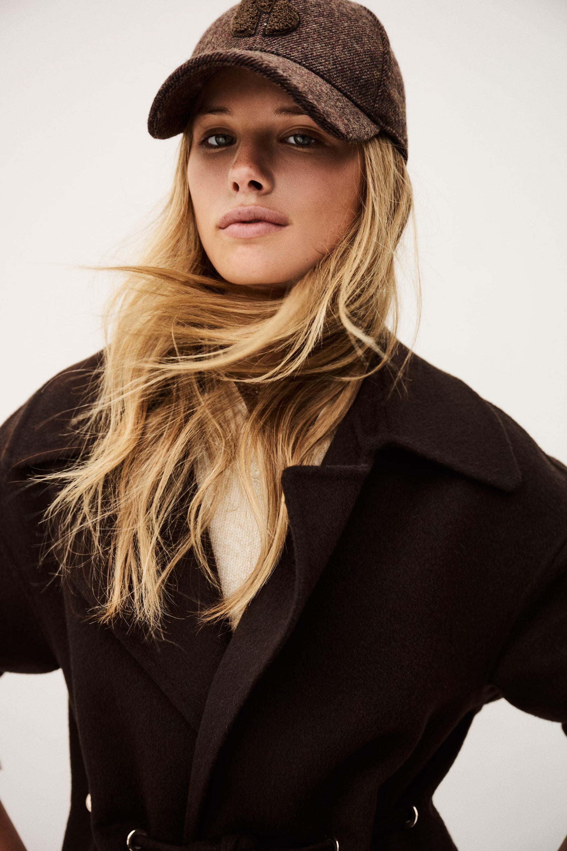 Woman wearing a brown coat and cap against a plain background