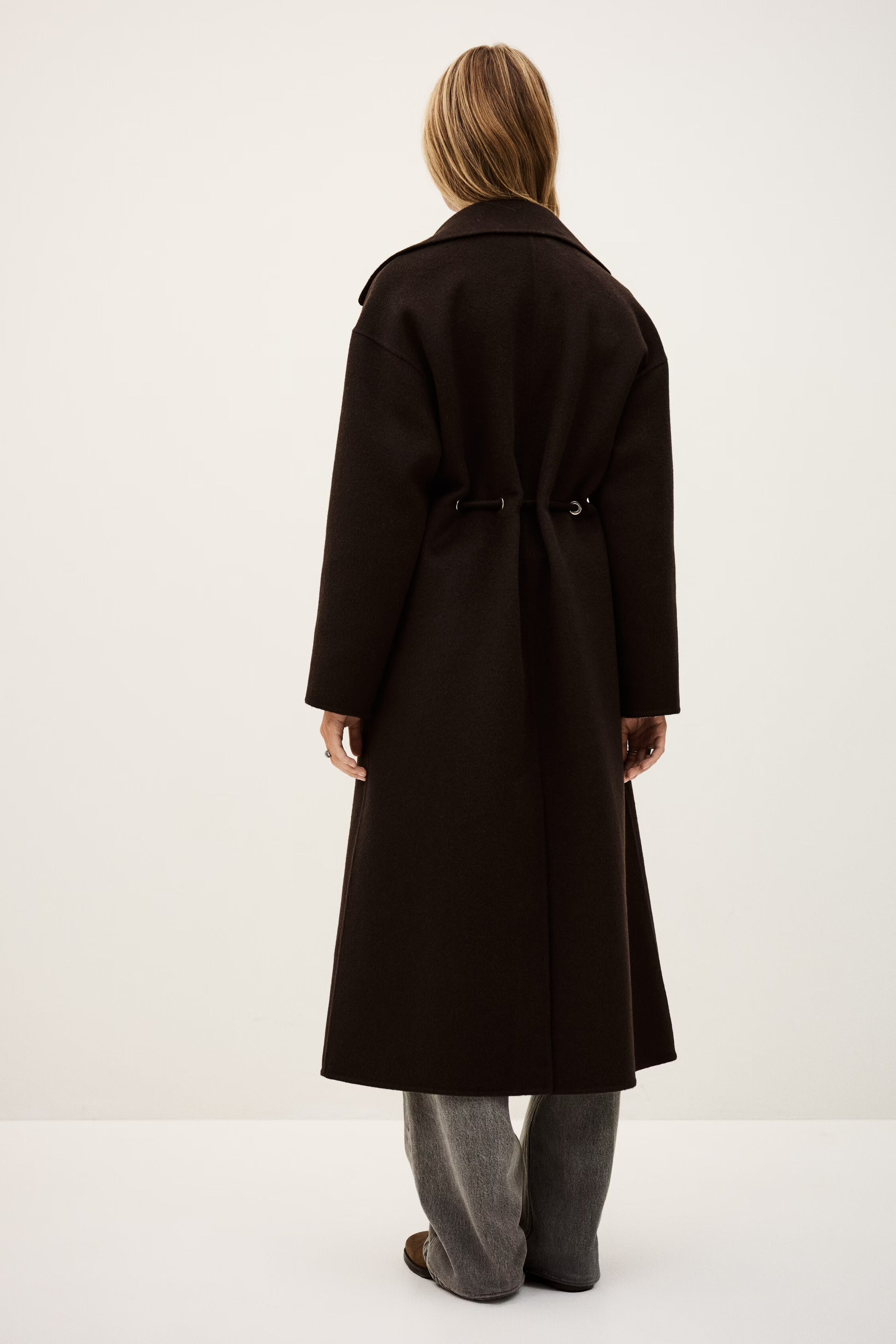 Person wearing a long black coat on a white background rear view