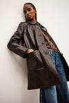 Person wearing a long dark coat over a brown shirt and blue jeans against a white background