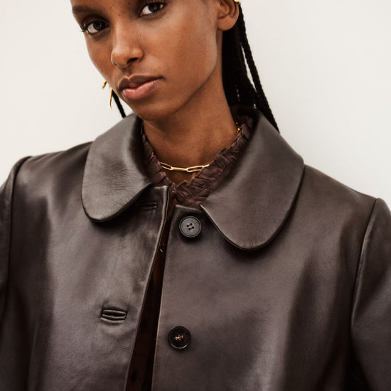 Woman wearing a brown leather coat with a neutral background