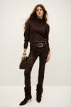 Woman wearing a brown turtleneck sweater, snake print pants, and black boots on a white background