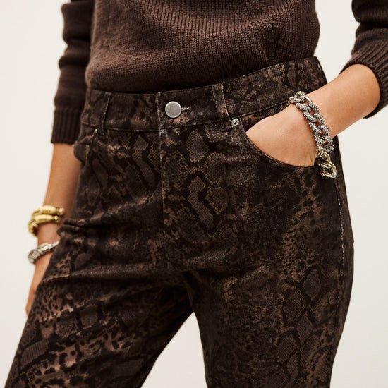 Person wearing brown sweater and snake print pants with a plain background
