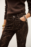 Person wearing brown sweater and snake print pants with a plain background