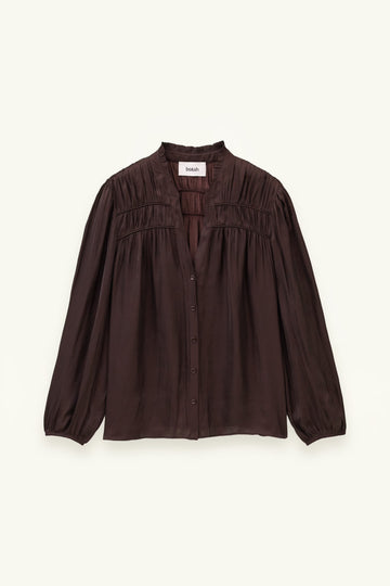 A dark brown long-sleeve blouse with a gathered, smocked bodice and button-front closure, displayed flat against a light cream background.