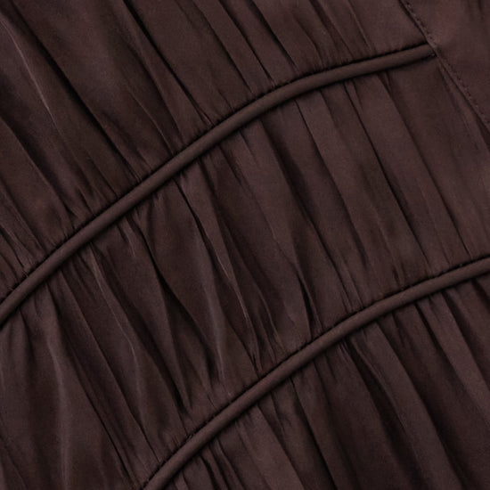 Close-up of a dark brown pleated fabric garment with gathered seams and a smooth satin-like finish.