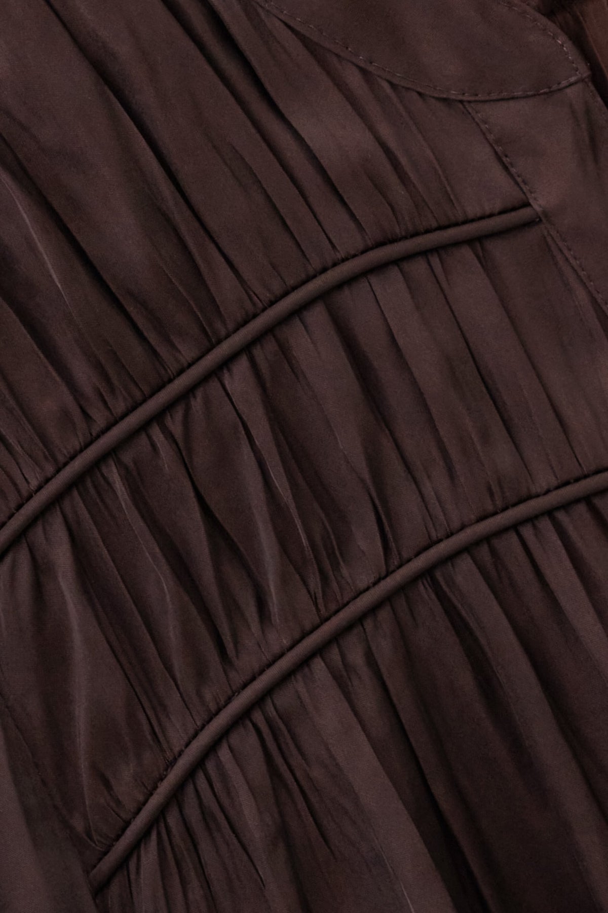 Close-up of a dark brown pleated fabric garment with gathered seams and a smooth satin-like finish.