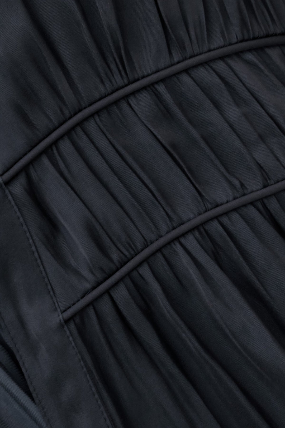 Close-up of a dark charcoal gray pleated fabric with curved seam lines.