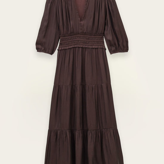 A dark brown tiered midi dress with three-quarter puff sleeves, a smocked waist, and a deep V-neckline, shown flat against a light beige background.